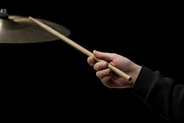 Hand of the musician with a drumstick on a black background