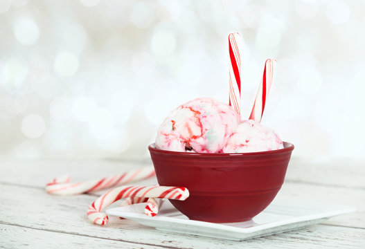 Peppermint ice cream and candy canes in a red bowl on white wooden table, soft holiday background