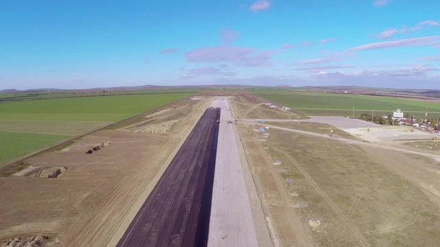 Tracked paver laying fresh asphalt pavement on an airport runway, aerial view
