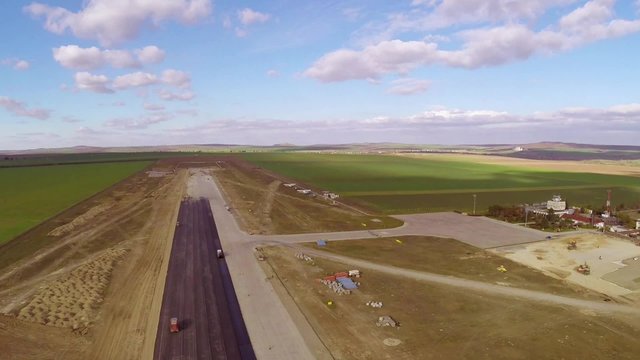 Tracked paver laying fresh asphalt pavement on an airport runway, aerial view
