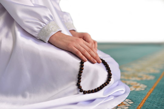 woman holding a rosary and praying in a white dress in a mosque on a white background