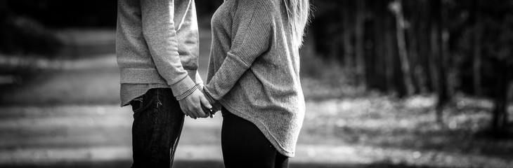 A hopeful young couple holding hands facing each other while stopped outside during a walk along a country road. - 95831285