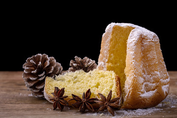 pandoro cake with icing sugar on wood with pine cone and star anise