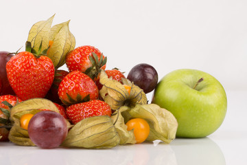 View of green apple with orange physalis, purple grapes and red strawberries on white background.