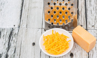 Grated cheddar cheese with steel grater over wooden background