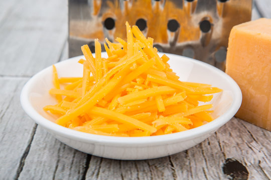 Grated cheddar cheese with steel grater over wooden background
