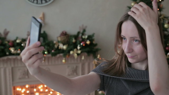Young pretty woman taking selfie at home while sitting near Christmas tree