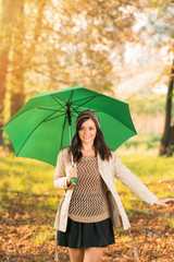 Happy young woman with umbrella in park in autumn