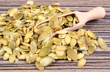 Pumpkin seeds with spoon on wooden background