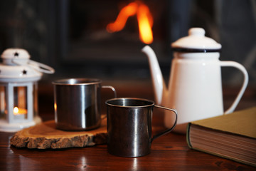 Teapot and mugs on vintage wooden table. Fireplace as background