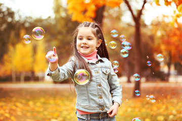 Cute girl playing with soap bubbles in park
