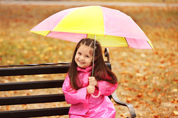 Beautiful little girl with umbrella sitting on bench in park