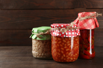 Jars with pickled vegetables and beans on wooden background