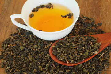 dry tea in wooden spoon with cup of tea on wooden background