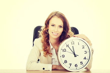 Businesswoman with clock by a desk.