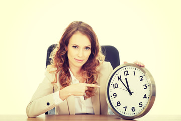 Businesswoman pointing on a clock by a desk.