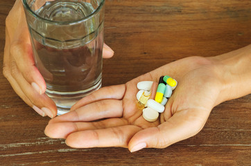 close up female hands holding pills, capsules, medicine,vitamin and water glass