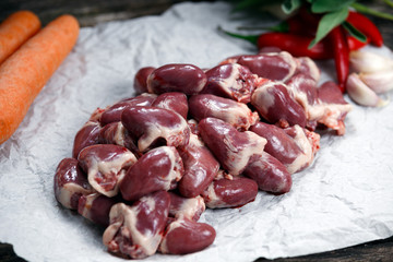 Raw Duck hearts on crumpled paper, decorated with vegetables. on old wooden table