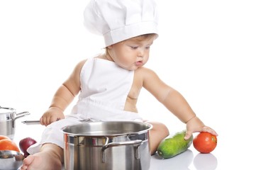 Funny adorable baby boy chef sitting and playing with kitchen equipment