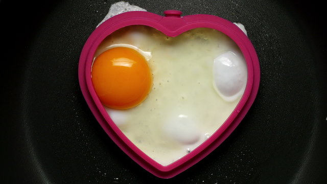 Cooking fried egg in the form of heart. Сlose-up 4K UHD 2160p footage.
