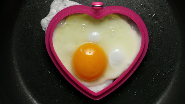 Cooking fried egg in the form of heart. Сlose-up 4K UHD 2160p footage.
