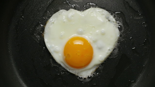 Cooking fried egg in the form of heart. Сlose-up 4K UHD 2160p footage.
