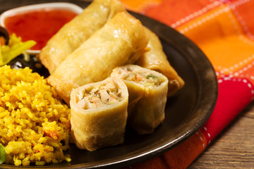 Portion baked spring rolls with vegetables and rice on a plate.