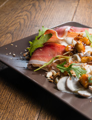 Decorate tagliatelle with cheese sauce, mushrooms and chicken. On top of this dish is arugula, prosciutto, ham and almonds. Everything is served on a plate and it is ready for consummation.