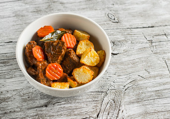 beef goulash with carrots and roasted potatoes in a white bowl on a light wooden background