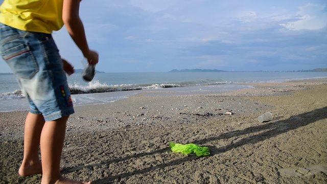 Young Asian boy collecting garbage on the beach near the ocean.