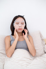 Woman sitting on bed and using the facial mask