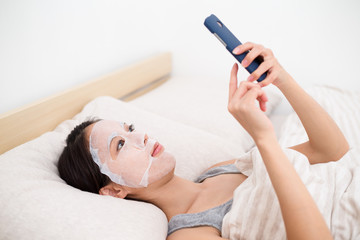 Woman using the facial mask and touch on the cellphone