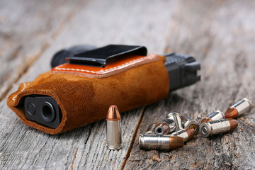 Automatic Handgun with leather holster and bullets on a wooden background.