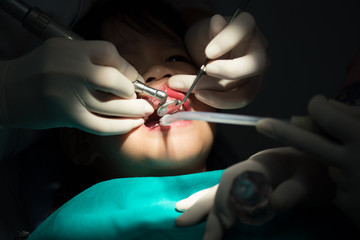 Dentist examining a patients teeth in the dentists chair under bright light