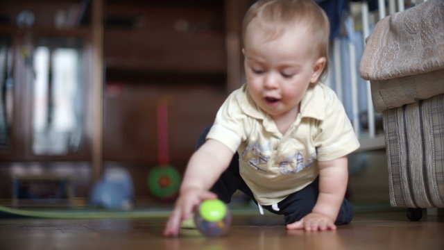 Little boy child play with the ball on the floor. Little boy sitting on the floor in a room and played the green ball. Boy have blond hair and a yellow shirt.