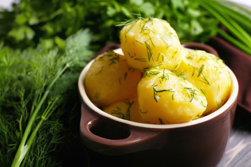 Boiled potatoes with greens in bowl on table close up