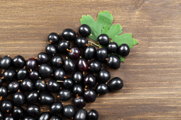 Heap of wild black currant with green leaves on wooden table close up