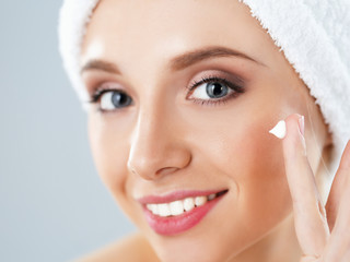 Beautiful young woman applying a creme on her face isolated on gray background