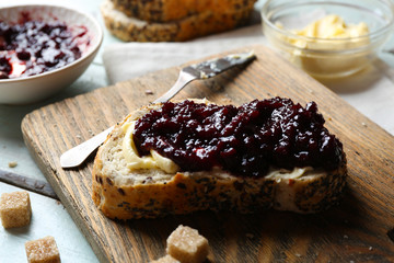 Tasty jam in the bowl, butter, fresh bread and crackers on blue wooden background