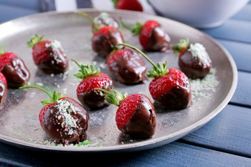 A plate of strawberries in chocolate on blue wooden background