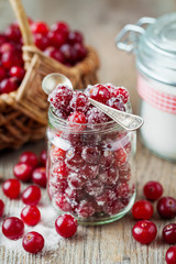 Cranberries with sugar in glass jar and basket with berries on background