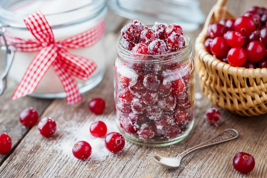 Cranberries with sugar in glass jar, basket with berries and sugar bowl 