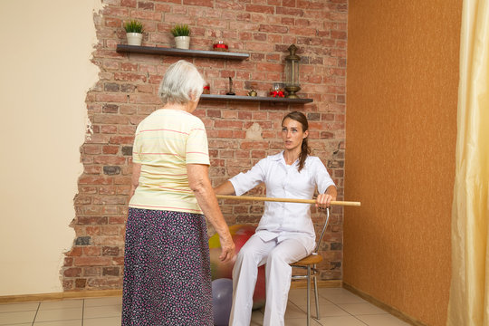 Physical Therapist Showing Exercise With A Stick For Senior Woman