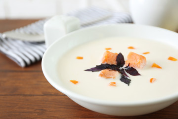 Delicious salmon cream soup in white plate on wooden table, close up