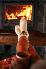Woman resting with cup of hot drink near fireplace