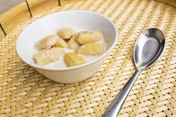 Banana in coconut milk serve in White bowl and spoon on basketry texture
