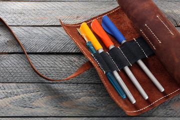 Leather case with items for drawing, on wooden background