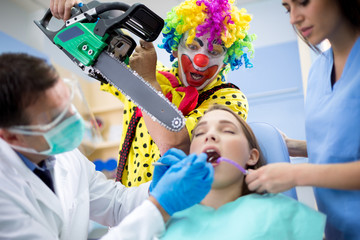 Clown threaten girl with chainsaw in dental ambulant - obrazy, fototapety, plakaty