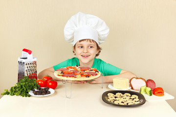 Little smiling boy in chefs hat preparing a pizza