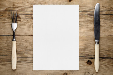 Blank paper for menu and fork and knife on wooden table